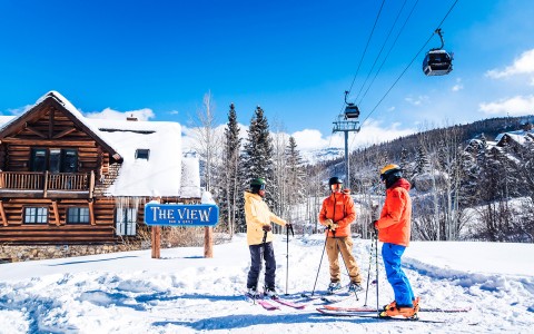 three skiers standing in front of the view restaurant during the day
