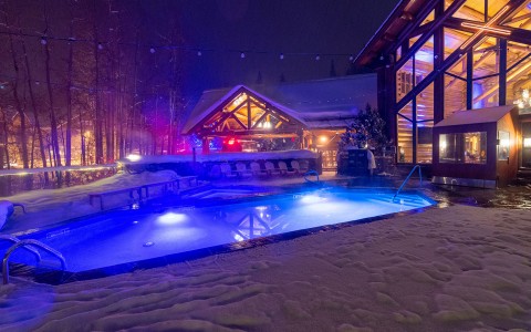 a pool with blue lights on and the lodge just behind it