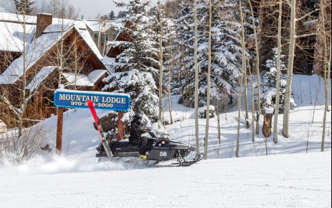 a person driving a black snowmobile in front of the mountain lodge