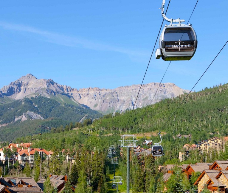 a gondola over the property with lots of green trees and mountains in the distance