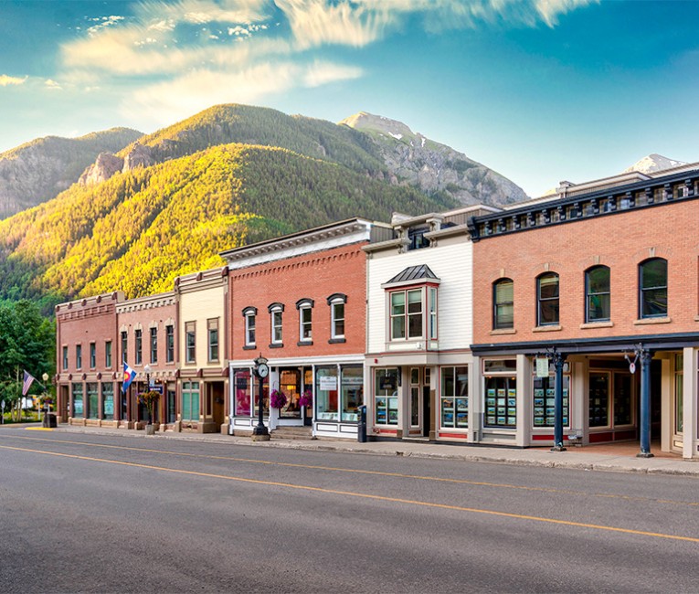 a row of businesses on main street with tall green mountains in the distance 