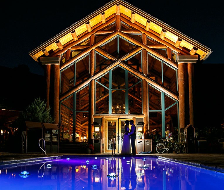 a bride and groom standing in front near the pool at night