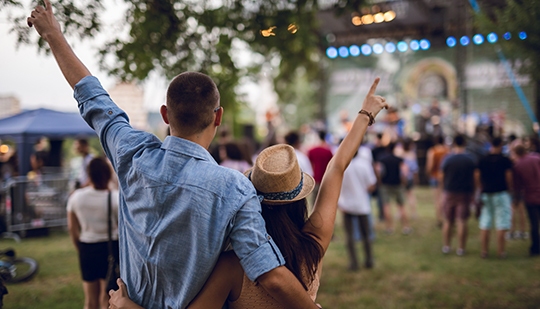 a group of people standing and watching a band perform outdoors at sunset