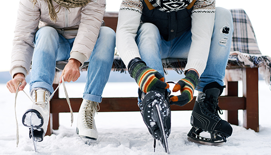 a close up of people tying their ice skates while sitting on a wooden bench