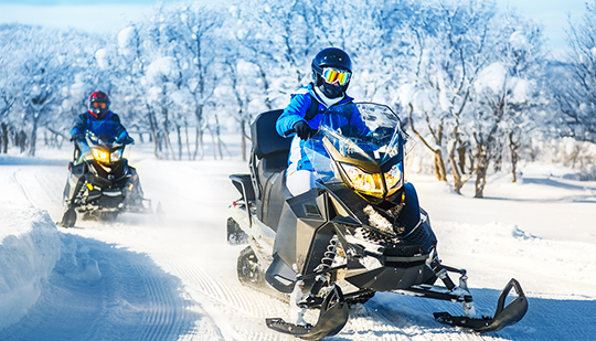 a person driving a black snowmobile through the snow with during the day