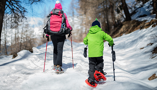 a kid and an adult walking through the snow in snowshoes during the day