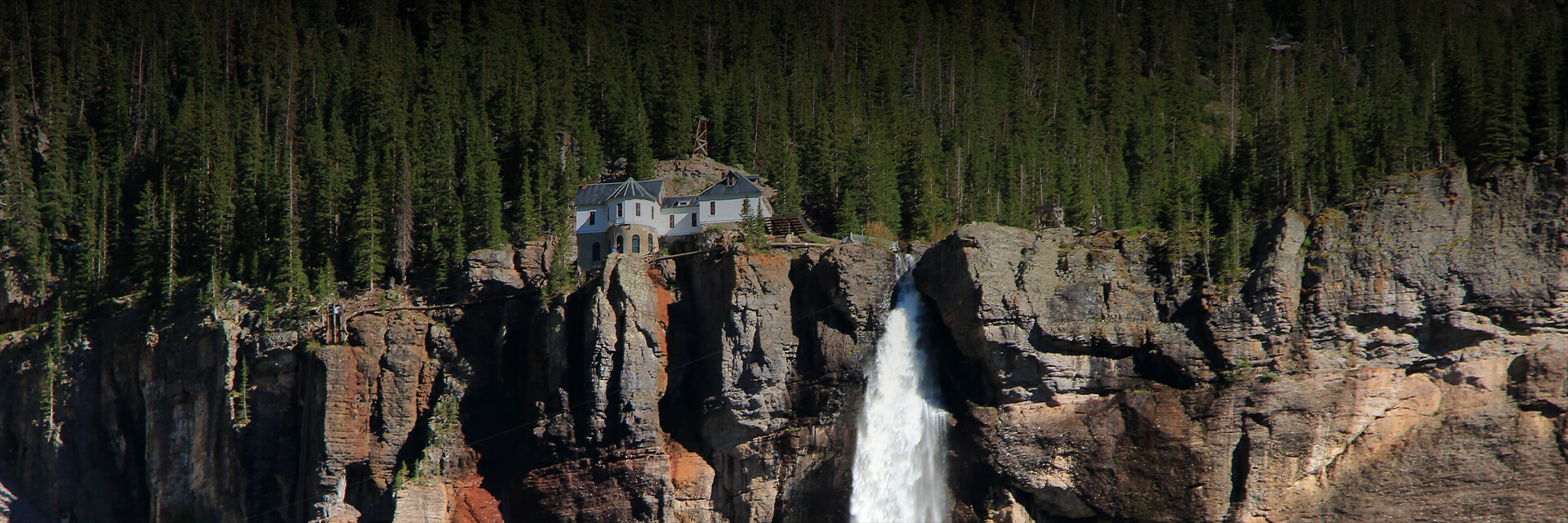 a panoramic view of a stone mountain with a waterfall and a home at the top