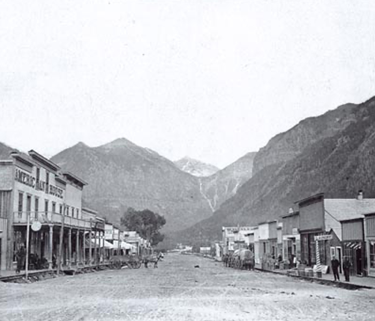 a black and white image of a small town with tall mountains in the background