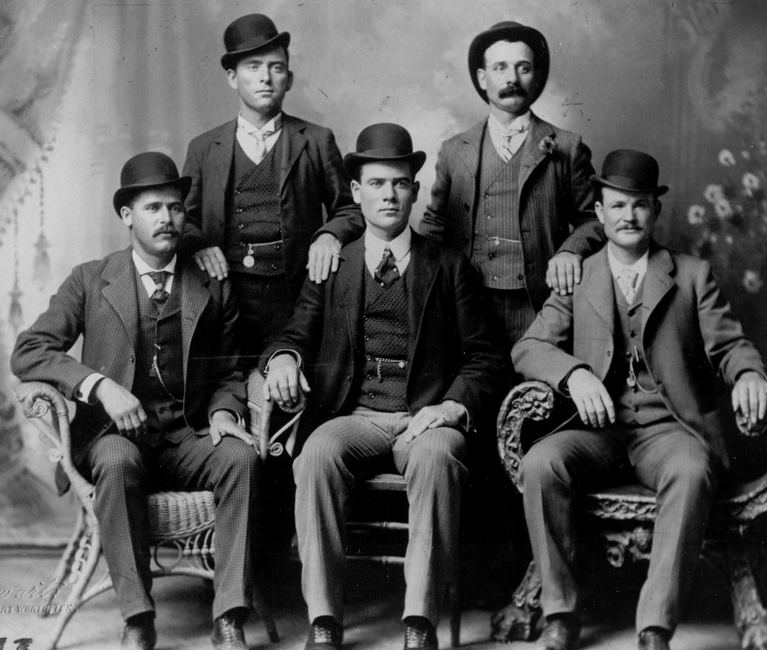 a black and white photo of men wearing suits and caps posing for a picture