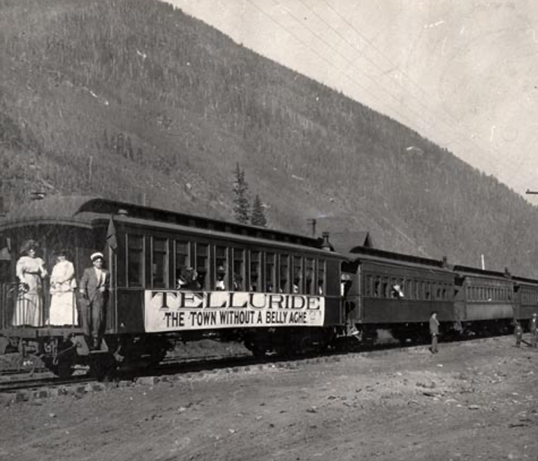 a black and white image of a train alongside a tall mountain
