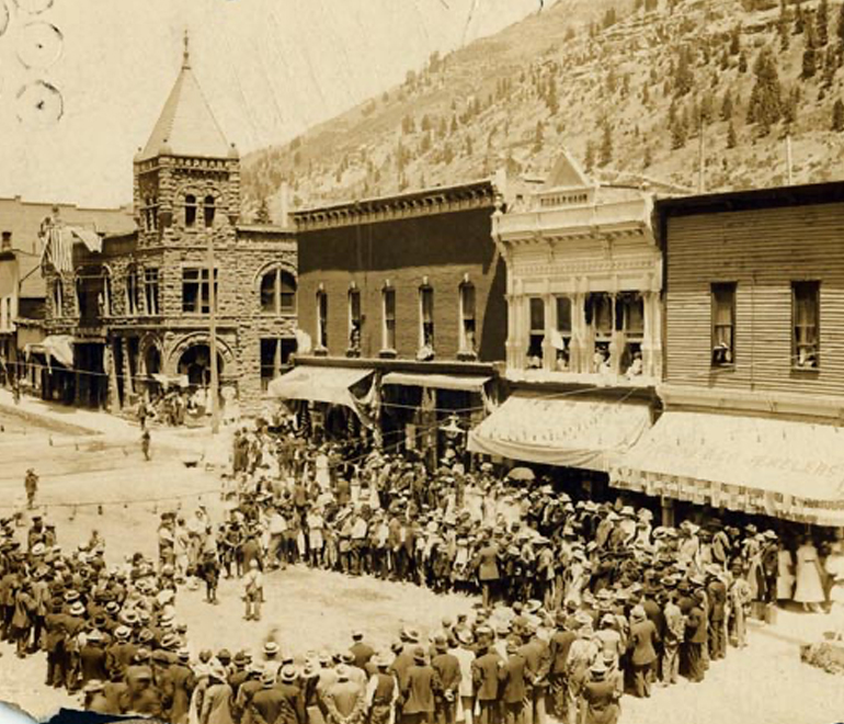 a black and white image of many people standing in line in front of an old store