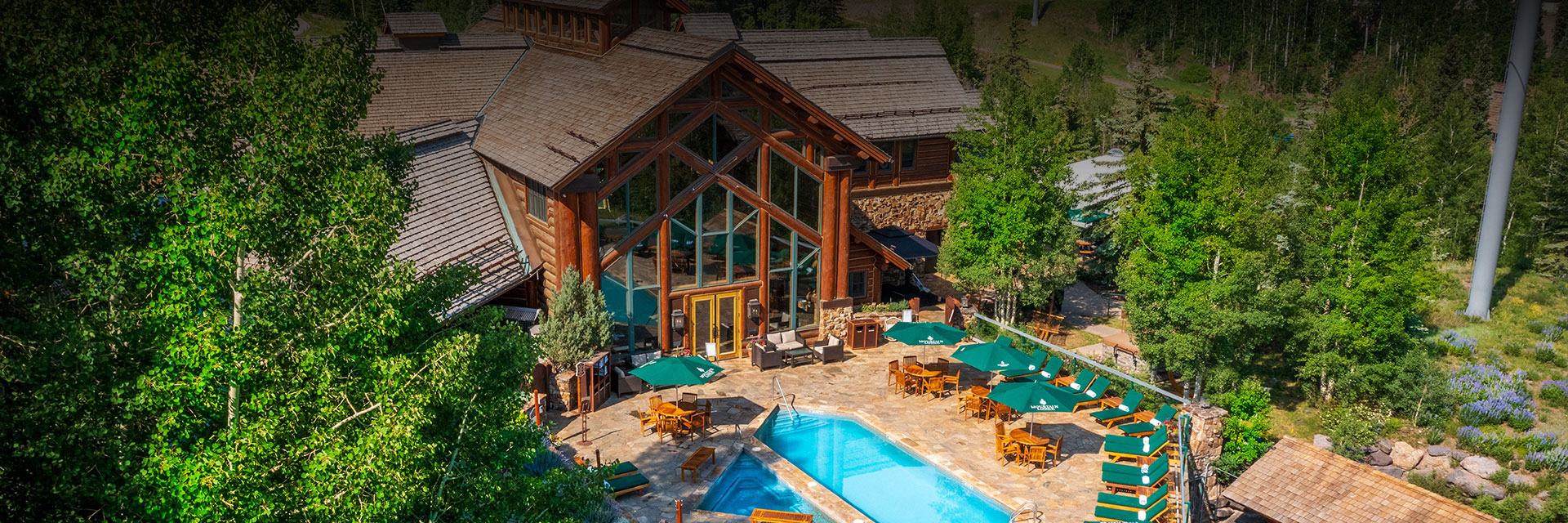 a view of the lodge and the pool area with tall green trees all around it