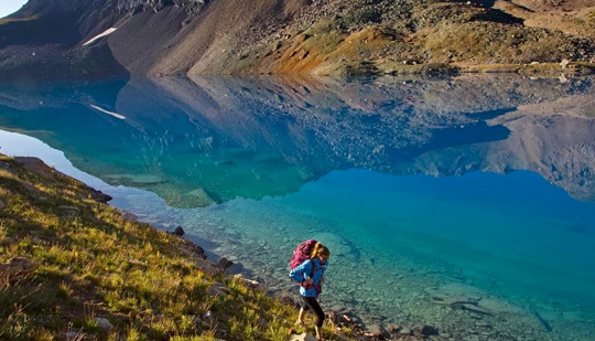 a woman hiking next to a clear blue river during the day