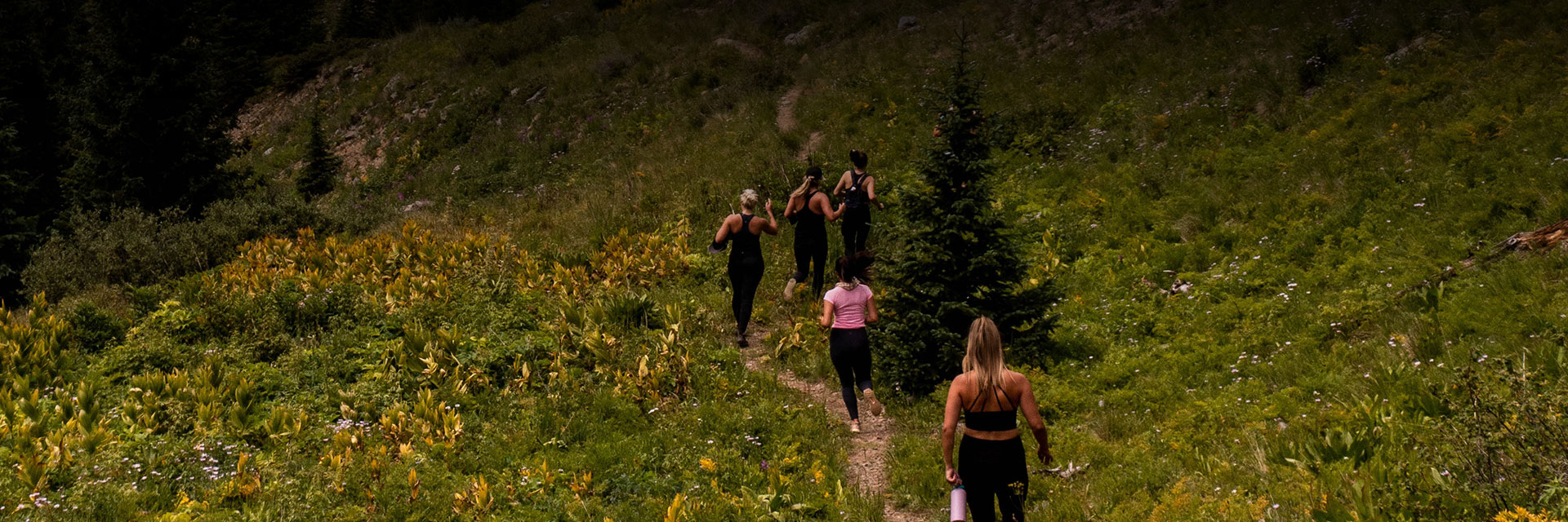 a group of women walking along a dirt trail surrounded by lush green landscape