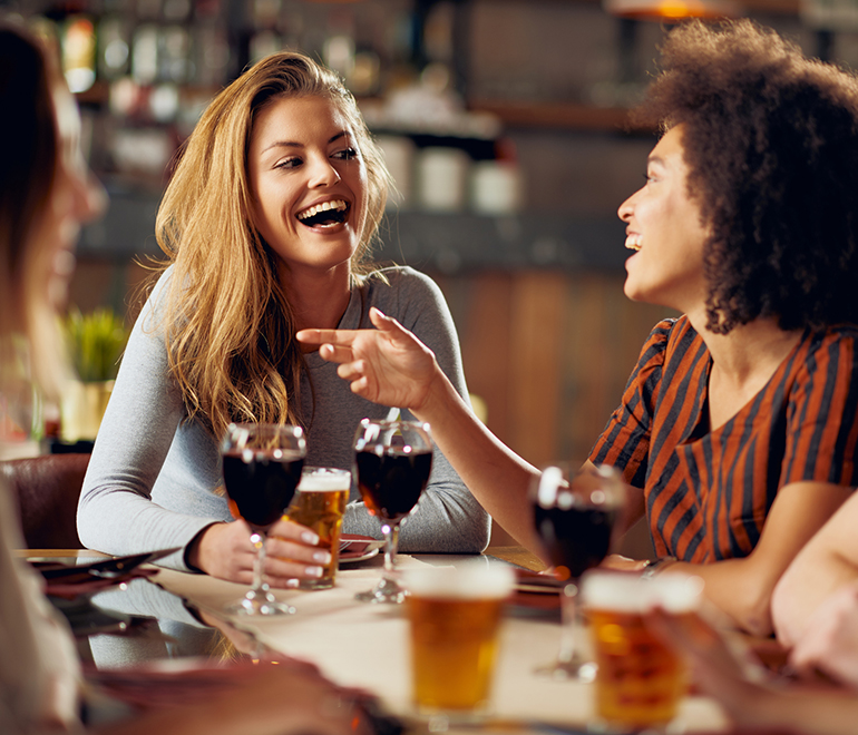 two smiling women drinking red wine and talking
