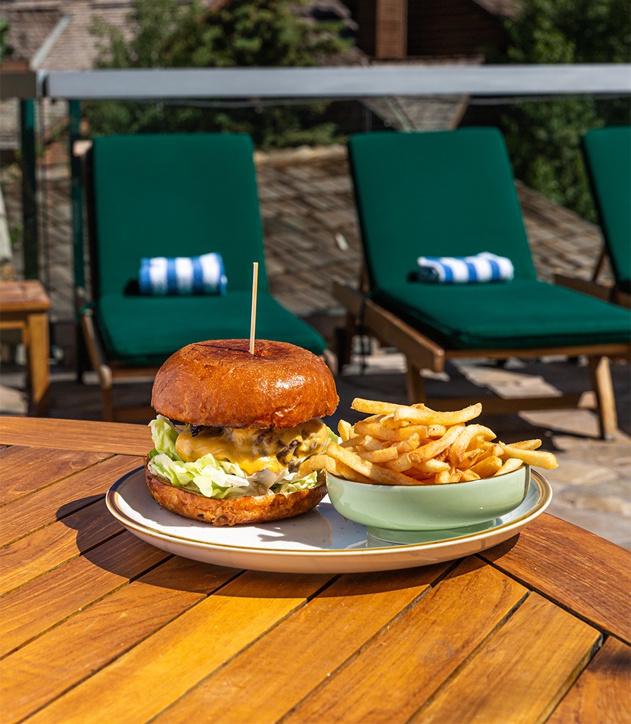 a cheeseburger and fries on a table with pool lounge chairs next to it