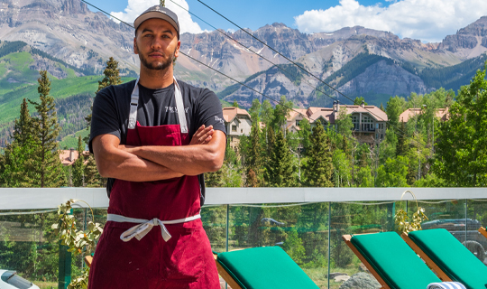 A man wearing an apron posing with his arms crossed on a pool deck during the day