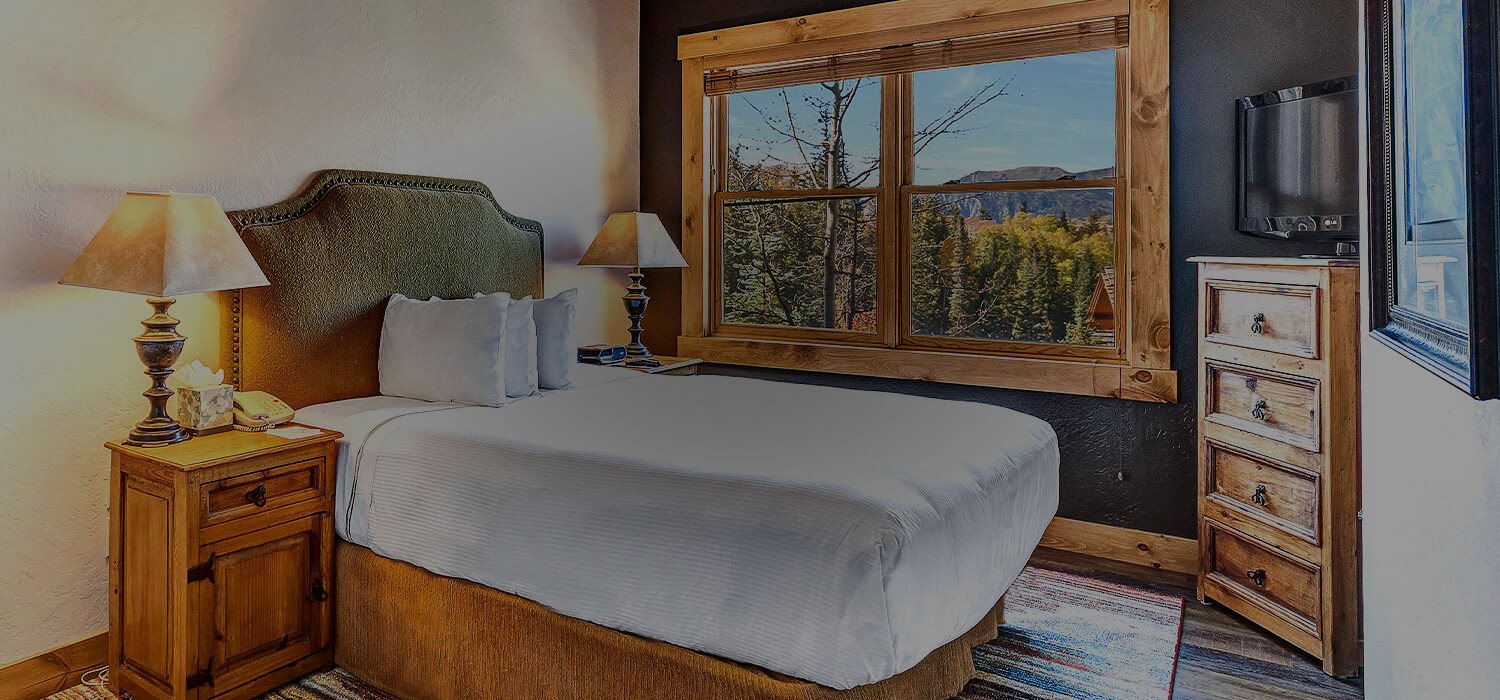 a bed in a room with lots of light wood furniture and a view of the mountains outside of the window