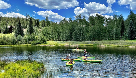 a group of people using green kayaks and paddle boards in a lake during the day