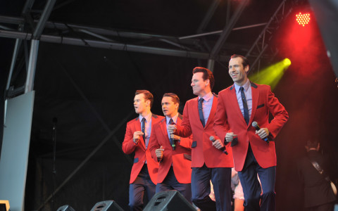 Cast of Jersey Boys in Red Sports coats dancing and singing on stage