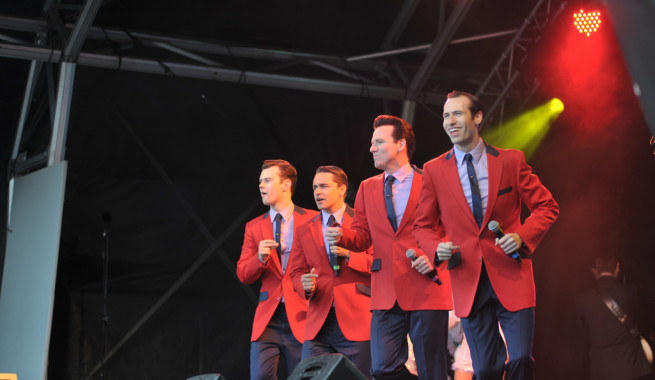 Cast of Jersey Boys in Red Sports coats dancing and singing on stage