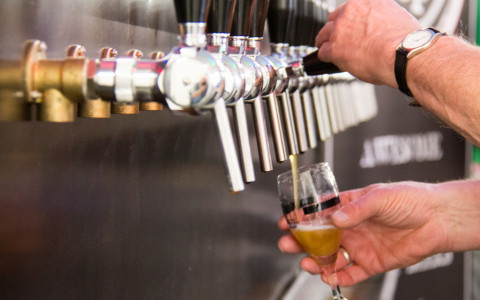 Hands pouring a beer from one of many silver taps
