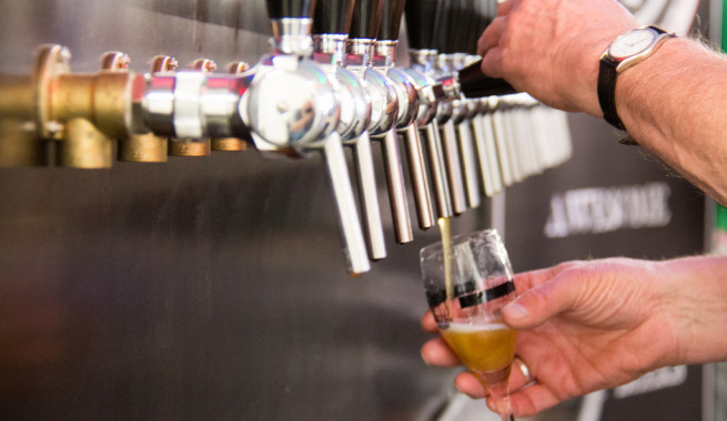 Hands pouring a beer from one of many silver taps