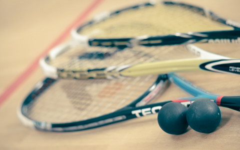 Three squash racquets and two squash balls on a squash court