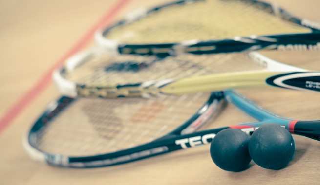 Three squash racquets and two squash balls on a squash court