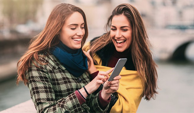 2 girls looking at a cell phone laughing