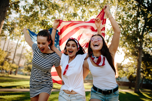 three girls running with an american flag in a park