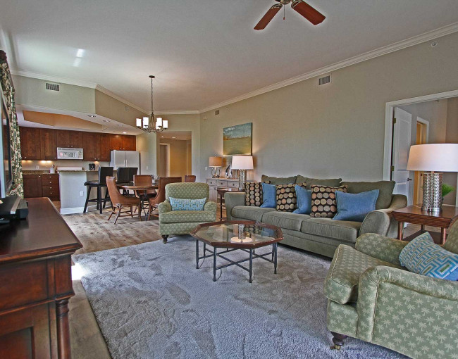living room area with a couch, two chairs, rug, coffee table, tv, and a view of the kitchen and dining area towards the door 