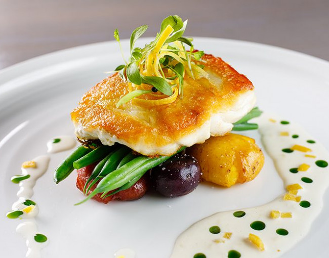 seared fish on top of colorful potatoes and green beans with sauce drizzled on the plate