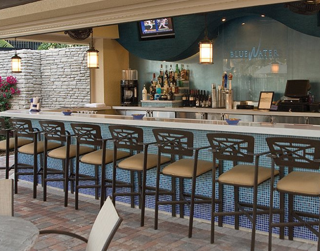 covered outdoor bar area with barstools and two televisions