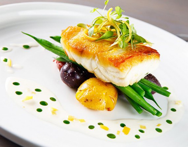 seared fish on top of colorful potatoes and green beans with sauce drizzled on the plate