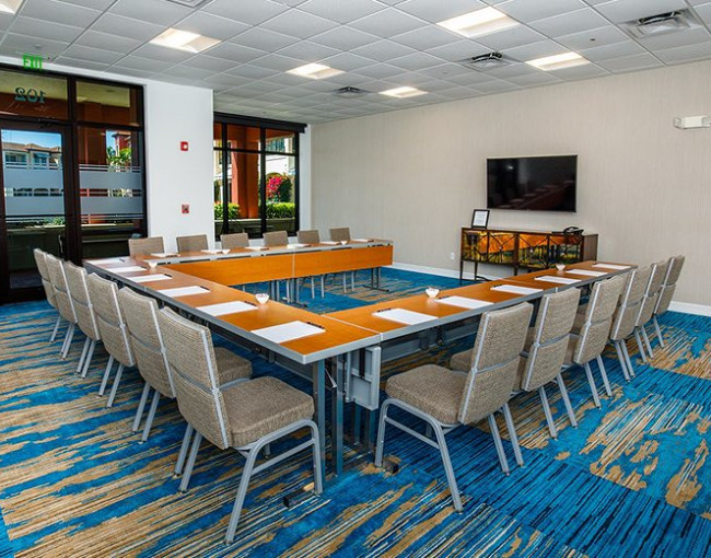 u-shaped conference table in a room with blue patterned carpet and a mounted tv on the wall