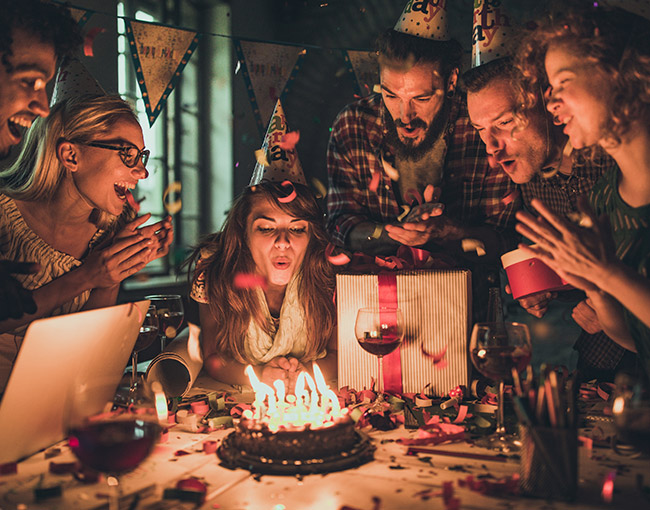 a woman blowing out her birthday cake candles surrounded by friends