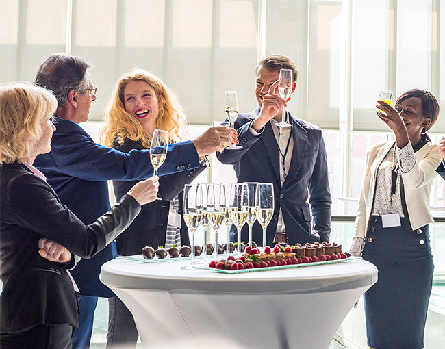 a group of business people standing around a cocktail tables holding up their glasses of champagne
