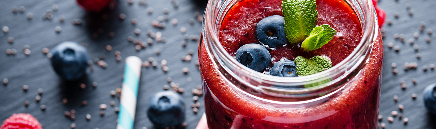 a pink fruit smoothie in a mason jar topped with blueberries and fresh basil