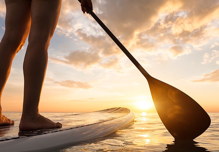 a woman standing on a paddleboard in the water at sunset