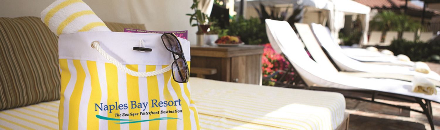a naples bay resort yellow and white striped beach bag sitting on an outdoor couch near lawn chairs
