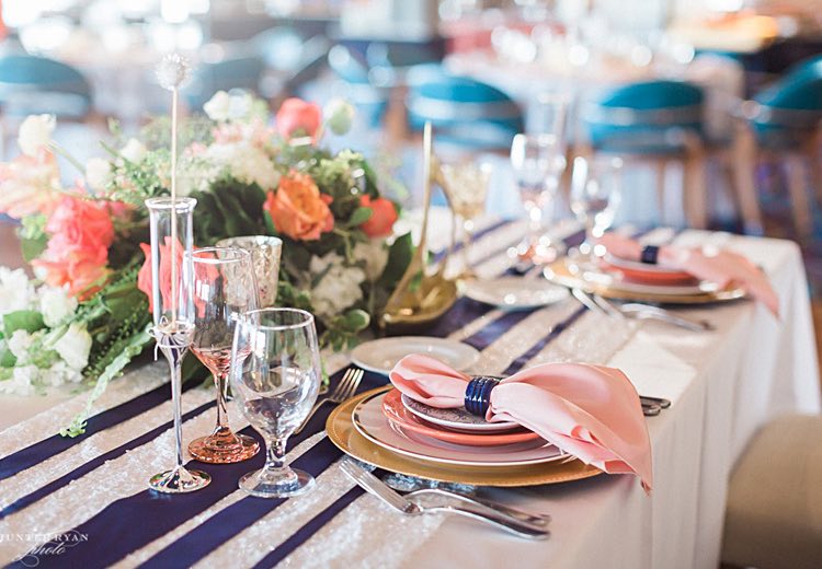 a buffet style table with glasses on champagne on gold serving stands, stacks of plates, small desserts on plates, and pitchers of water