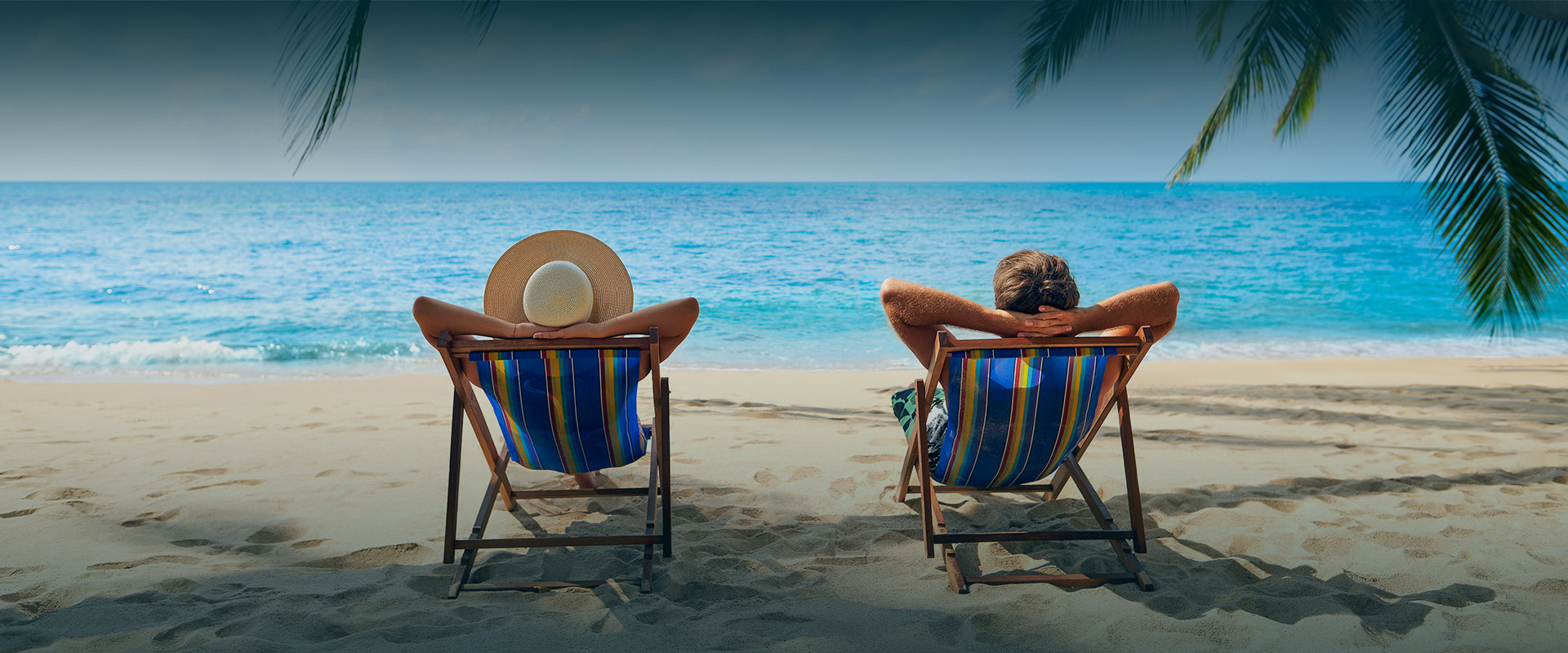 Back view of two people relaxing on beach chairs next to a seashore
