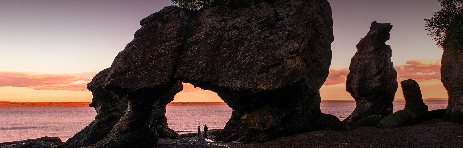 large boulders overlooking the ocean with a pink and yellow sunset in the background