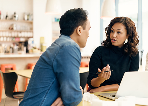 Woman and man sitting in cafe working on their laptop speaking to each other