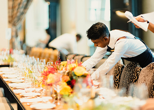 waiter setting up large decorated table with plates and center pieces 