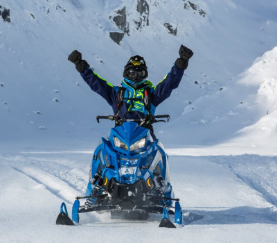 person with raised hands riding blue snowmobile