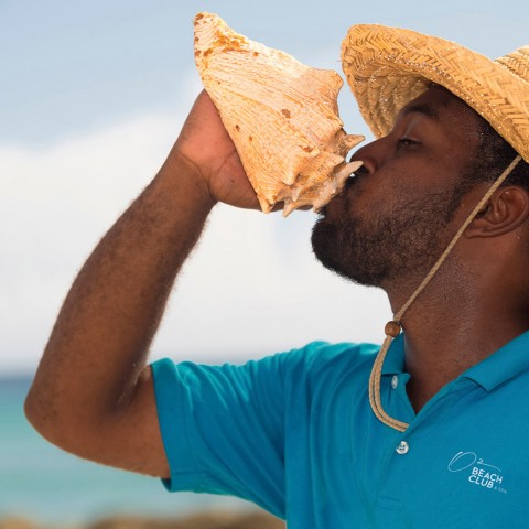 man blowing into conch shell