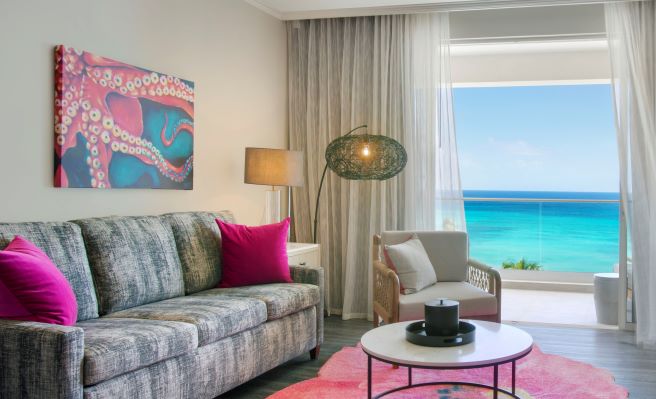 guest room with grey couch and hot pink pillows with a view overlooking the ocean