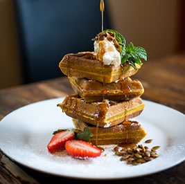 syrup being poured over a stack of waffles